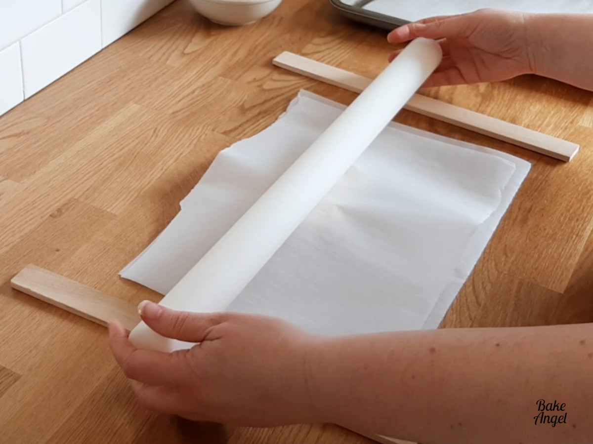 Rolling out cookie dough between parchment paper and using paint stirrers as guide sticks. 