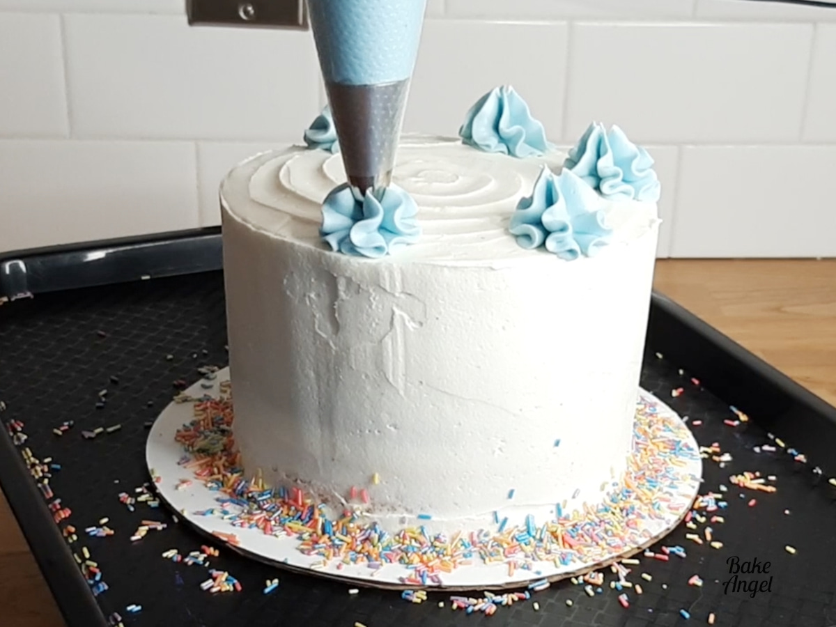 Piping a blue buttercream swirl on top of the cake. 