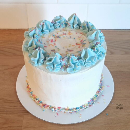 A fully decorated vegan vanilla layer cake with buttercream swirls and sprinkles