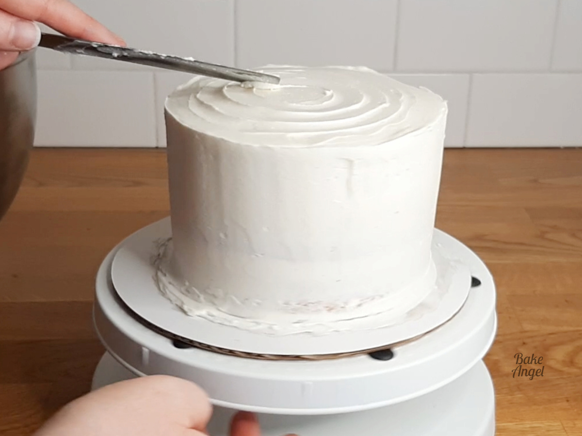 Showing a spatula dragging through the buttercream to draw a spiral on the top of the cake.
