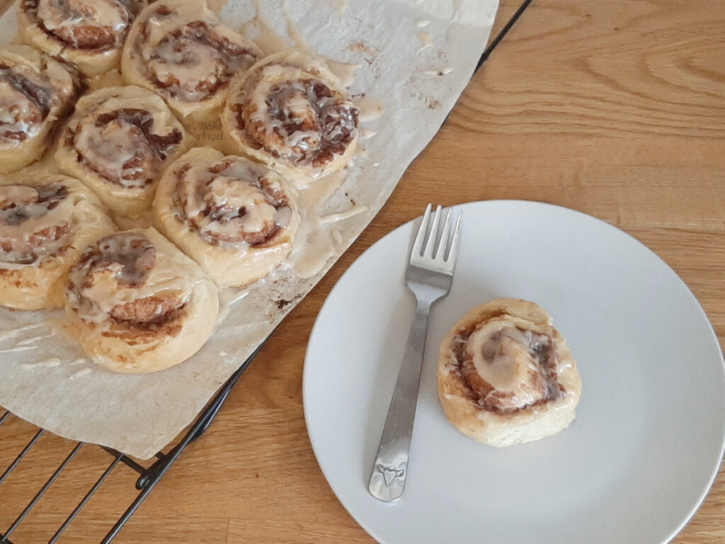 A batch of brown sugar cinnamon rolls on parchment paper, next to one cinnamon roll on a white plate with a fork. One of the Best Vegan Thanksgiving Desserts from my roundup.