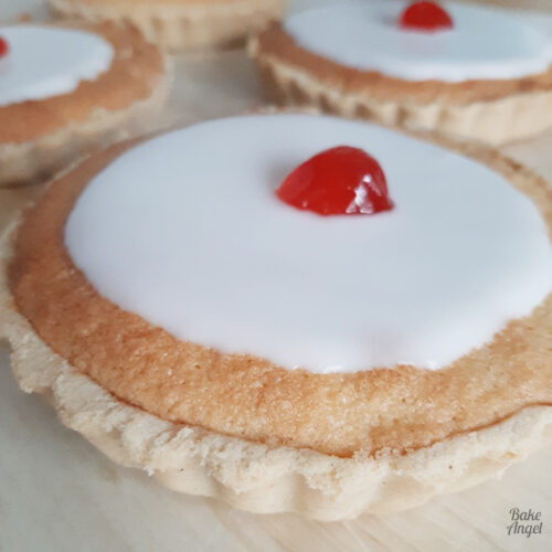 Close up of a mini cherry bakewell tart on a wooden board.