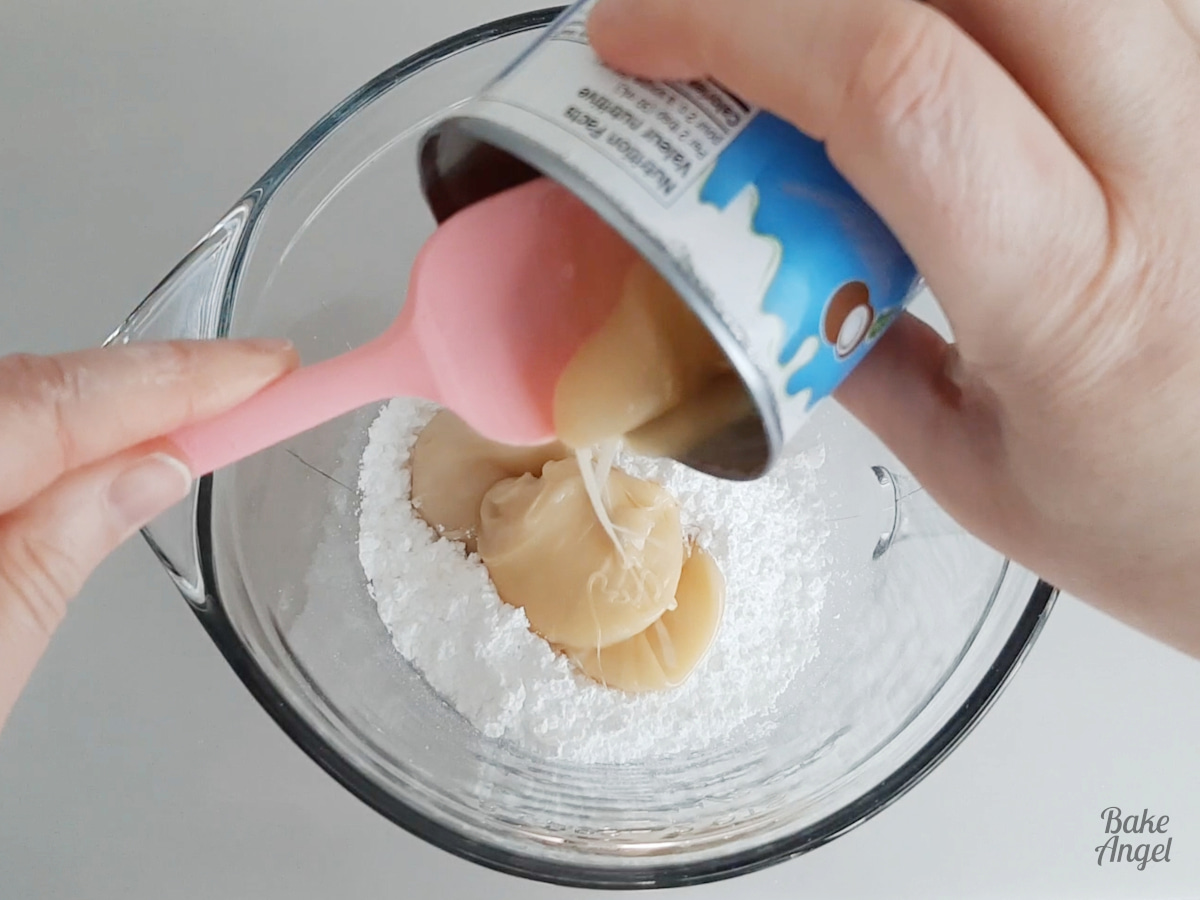 Adding condensed coconut milk to a bowl of icing sugar and using a pink spatula. 
