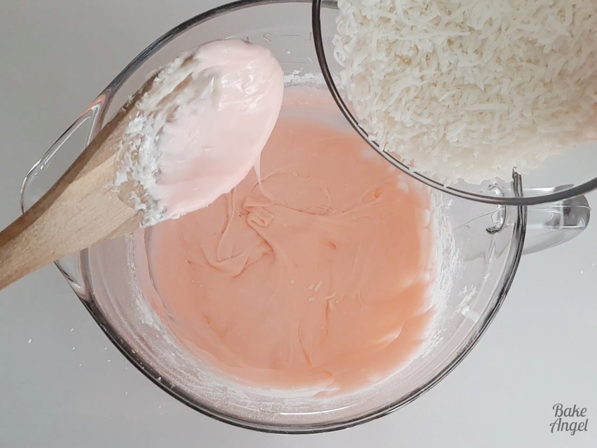 Adding a bowl of shredded coconut to the pink condensed coconut milk mixture. 