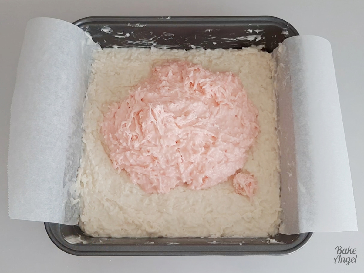 The pink coconut ice in a heap on top of the white coconut ice in a baking pan. 