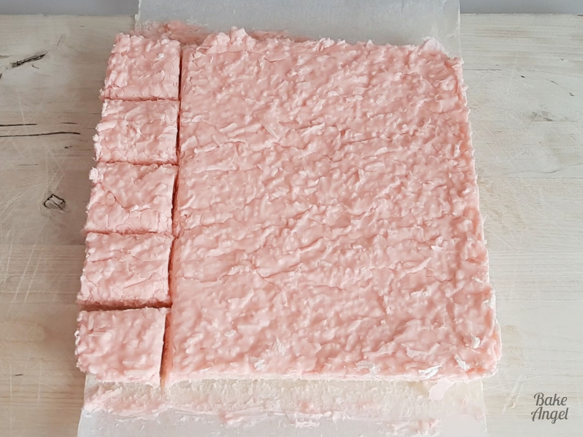 A slab of coconut ice on a wooden board with 5 squares cut on the left side. 
