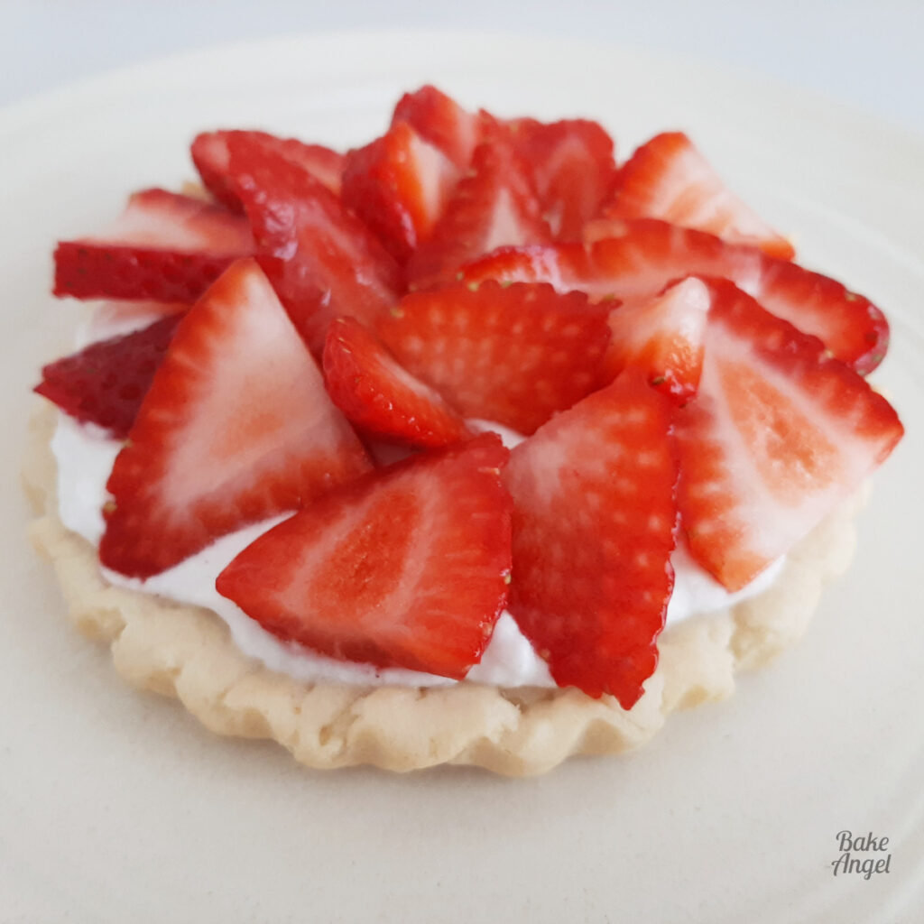 Side view of a mini strawberry whipped cream tart on a light beige plate.
