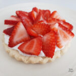 Side view of a mini strawberry whipped cream tart on a light beige plate.