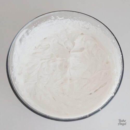 A freshly made bowl of vegan whipped cream icing on a white counter.