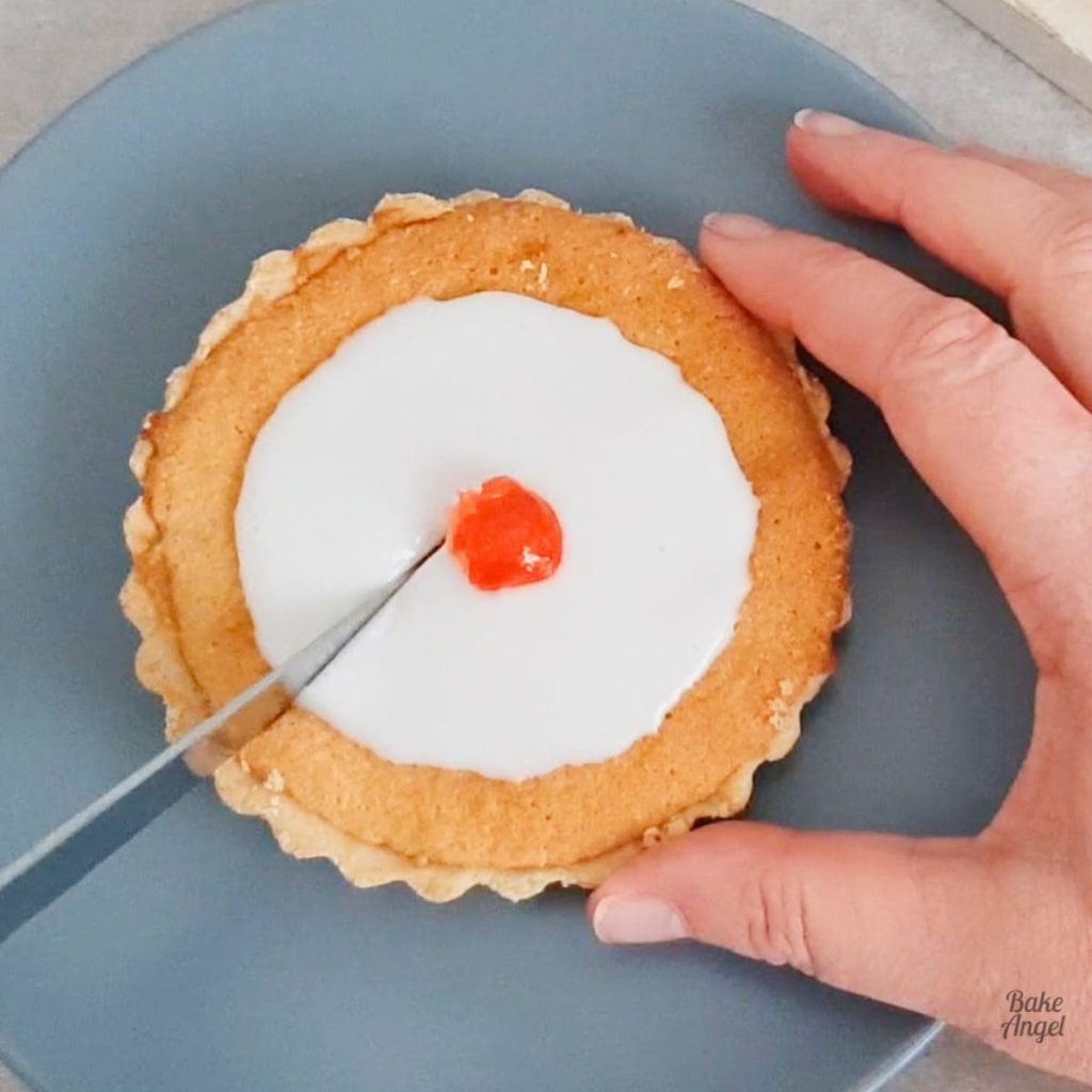 A mini gluten free dairy free cherry bakewell tart being cut while one hand holds it.