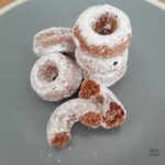 A stack of mini chocolate donuts dusted with icing sugar on a blue plate.
