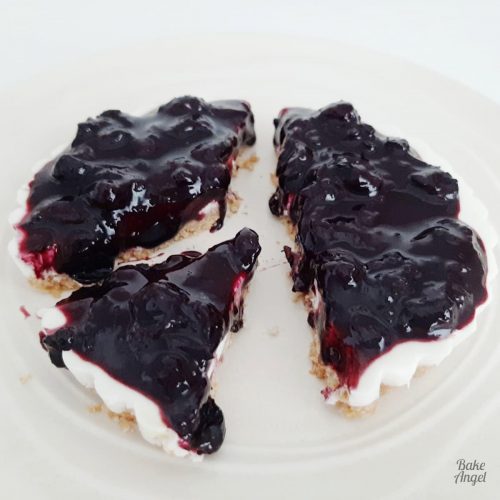 A mini vegan blueberry cheesecake topped with blueberry compotecut in to 3 portions on a cream plate.