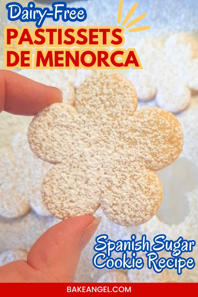 A dairy-free pastisset de menorca sugar cookie being held over a tray of baked cooked drenched in icing sugar.