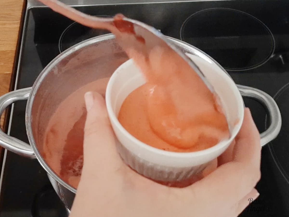 Removing foam from the jam with a ladle and putting it in to a white ramekin. 