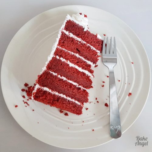 A slice of red velvey layer cake on a white plate with a silver fork.
