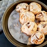 7 cinnamon rolls topped with maple glaze in a round cake pan.