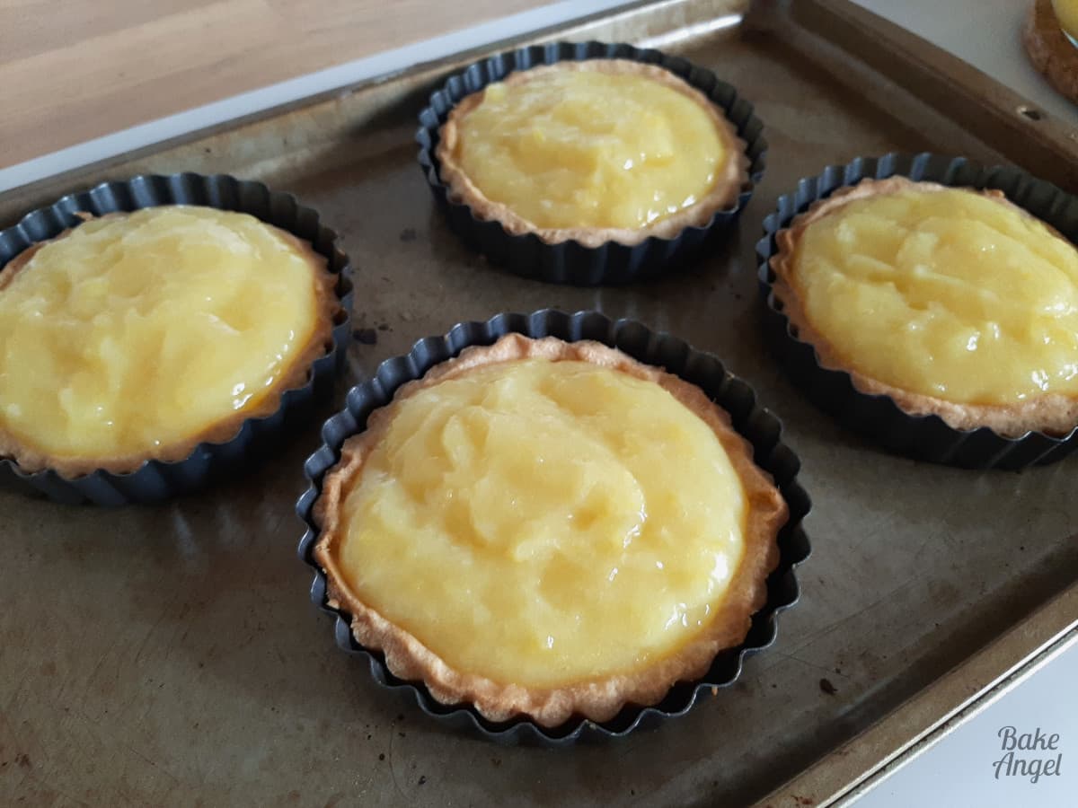 4 mini tart cases filled with lemon pie filling on a baking tray. 