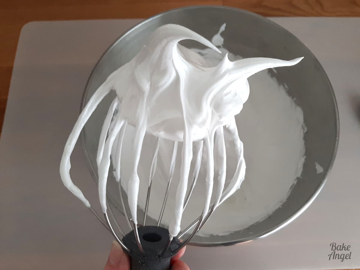 Stiff meringue on a whisk held over a bowl. 