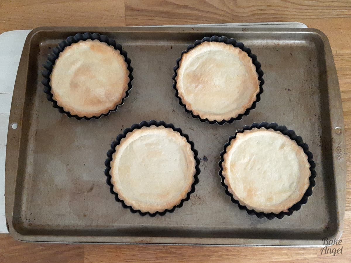 4 mini pastry bases on a baking tray after baking, showing the golden colour  in the pastry. 