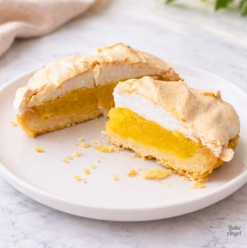 Close up of a slice of dairy-free lemon meringue pie on a white plate with crumbs nearby.