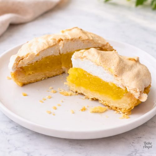 Close up of a slice of dairy-free lemon meringue pie on a white plate with crumbs nearby.