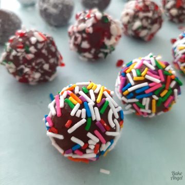 Close up of a cheesecake truffle coated in rainbow sprinkles with candy cane coated truffles in the background.