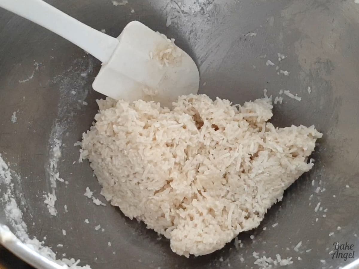 Coconut macaroon mixture folded together in a mixing bowl with a white spatula. 