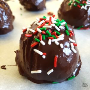 Close up of a festive cake ball coated in chocolate with white, green and red sprinkles on top.