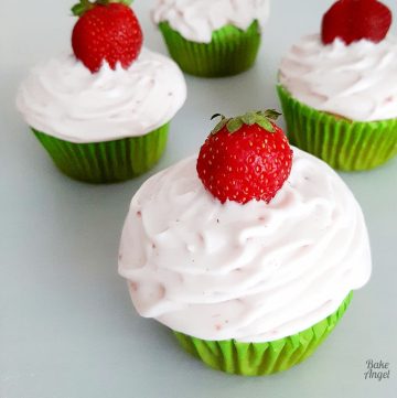 Close up of strawberry cream cheese frosting on a cupcake topped with a fresh strawberry.