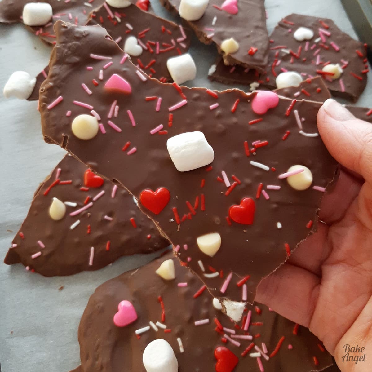 Close up of a piece of Valentines Bark being held. There are sprinkles, white marshmallows, and heart candies in the chocolate.