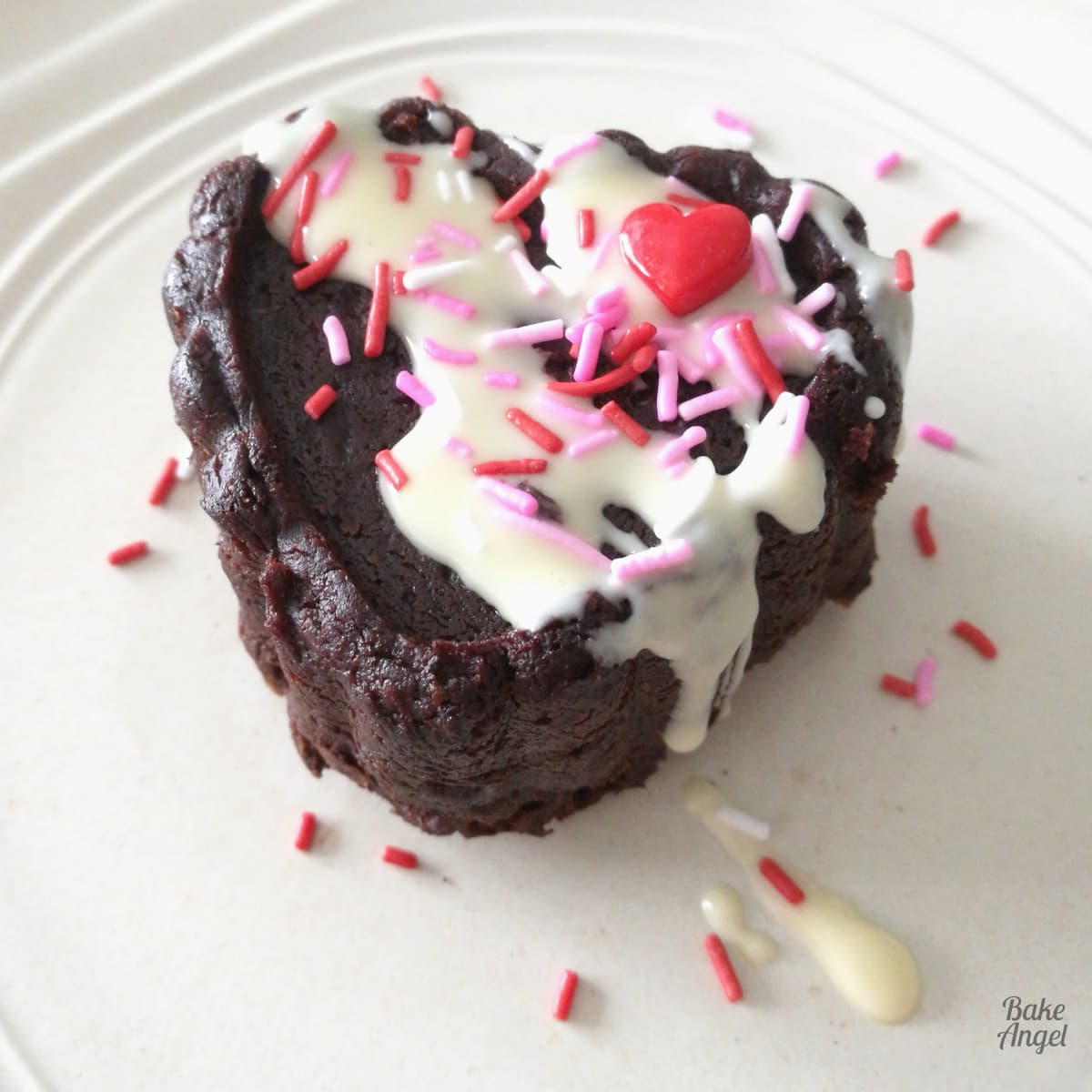 A mini heart brownies on a plate and decorated with melted white chocolate and pink, red and white sprinkles.