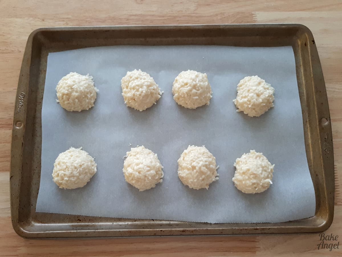 8 coconut bliss balls on a baking tray lined with parchment paper. 