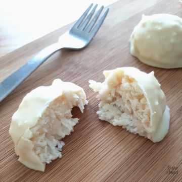 A vegan white chocolate coconut bliss ball cut in half on a wooden board with a fork in the background.