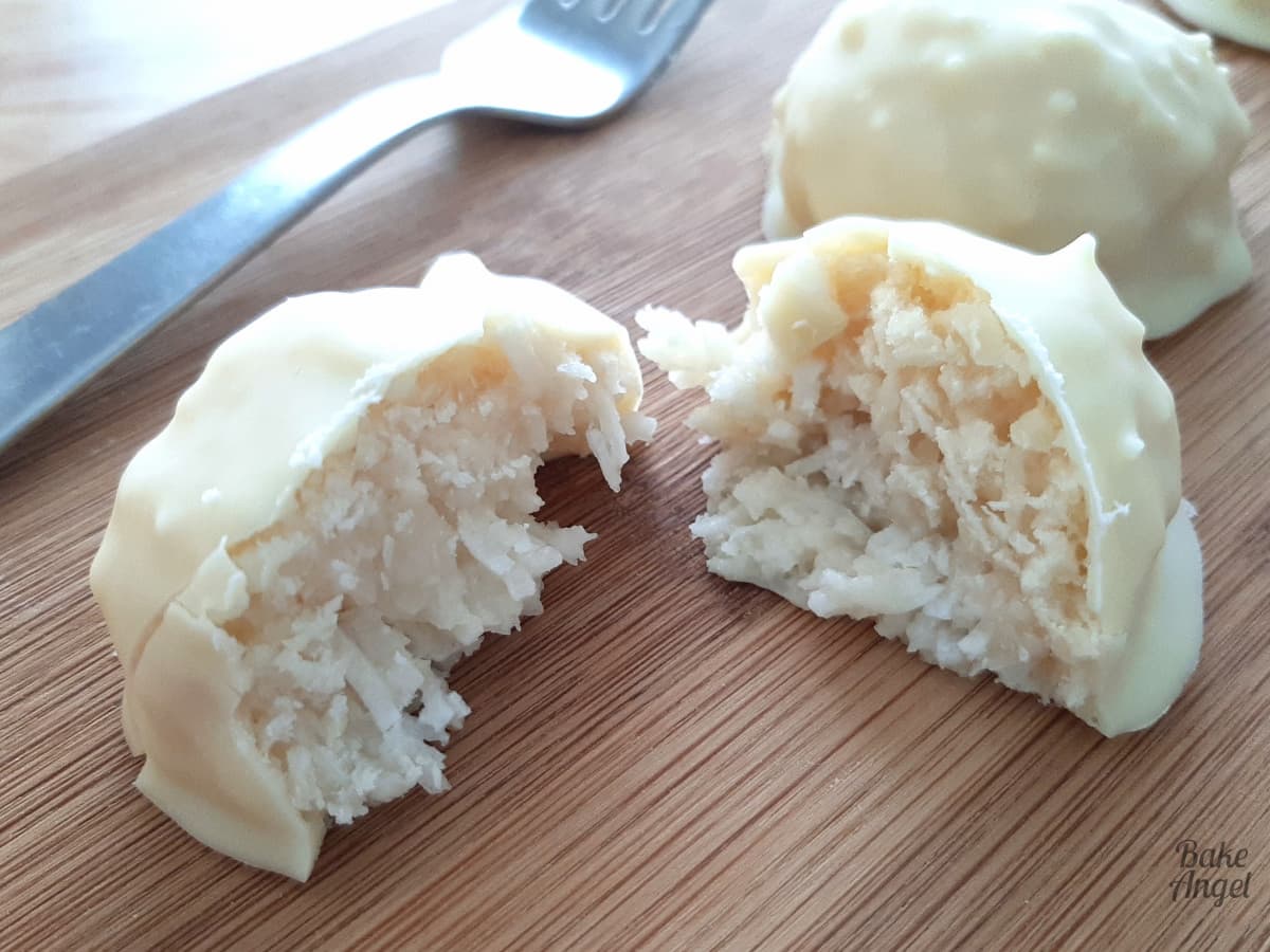 A vegan white chocolate coconut bliss ball cut in half on a wooden board with a fork in the background. 