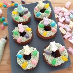 6 Easter Donts on a blue plate and decorated with pastel green buttercream, jelly beans and bunny marshmallows.