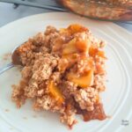 Close up of gluten free vegan peach crumble on a white plate.
