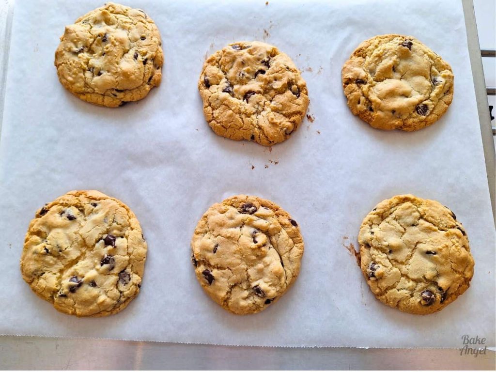 6 baked copycat Disney chocolate chip cookies on parchment paper on an airbake tray.
