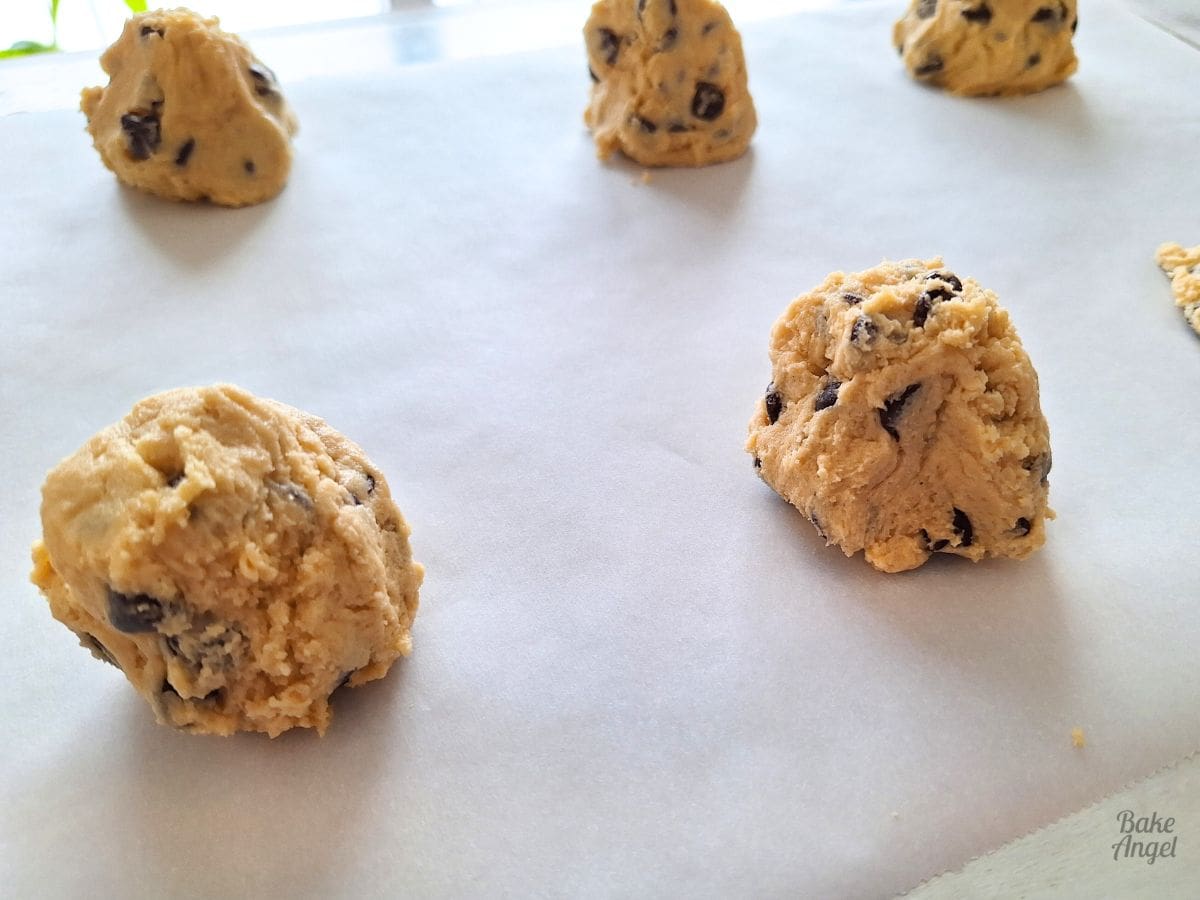 Close up of small stacks of cookie dough on parchment paper before baking.