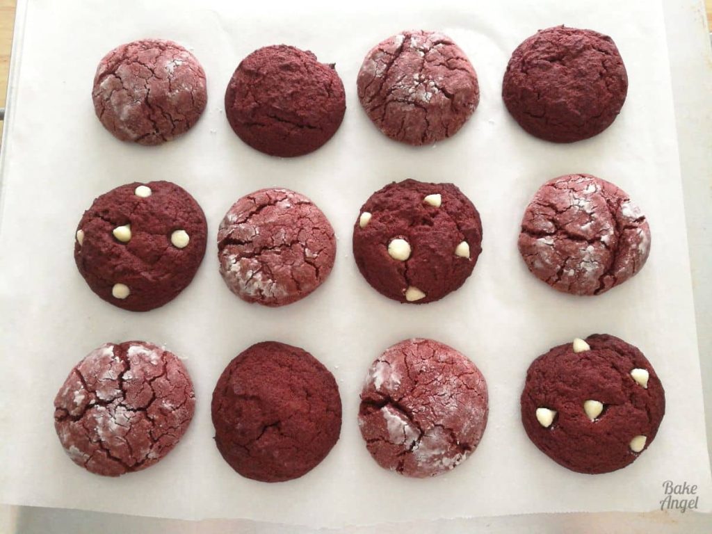 12 baked red velvet cookies on parchment paper on a baking tray.
