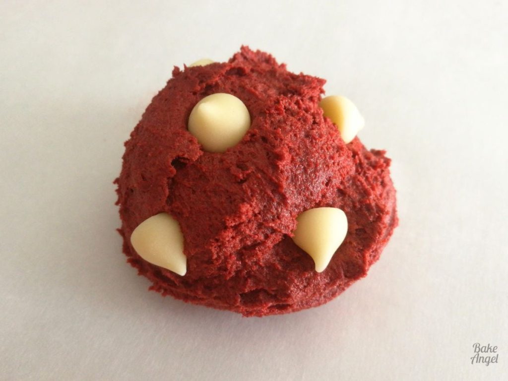 Close up of a ball of red velvet cookie dough with white chocolate chips pressed in to it.