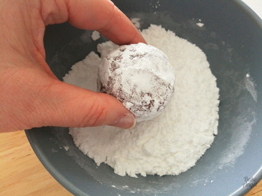 A ball of red velvet cookie dough covered in icing sugar over a bowl of icing sugar.