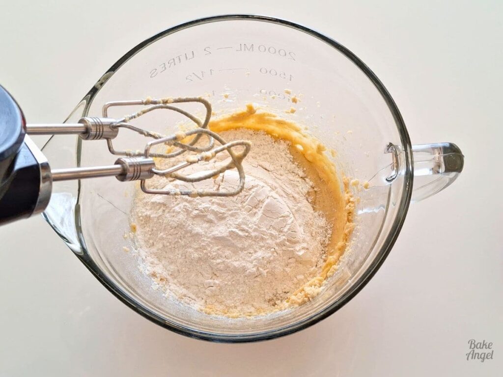 Ingredients in a mixing bowl to make a small batch of funfetti cookies. A hand mixer is above the bowl.
