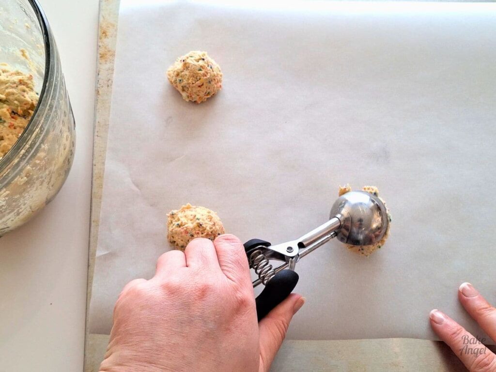 A scoop being used to add funfetti cookie dough balls to parchment paper.