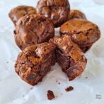 A close up of a two bite brownie cut in half with crumbs in front of it.