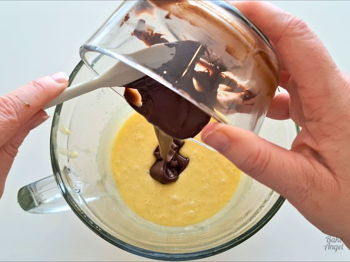 Melted chocolate being drizzled in to a glass mixing bowl containing mixed ingredients.
