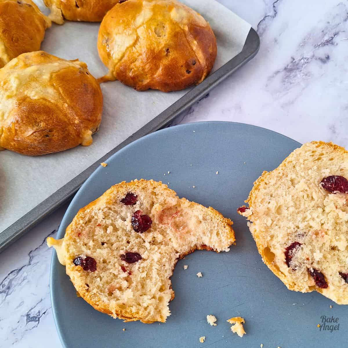 Close up of a white chocolate cranberry hot cross bun, split in half on a blue plate.