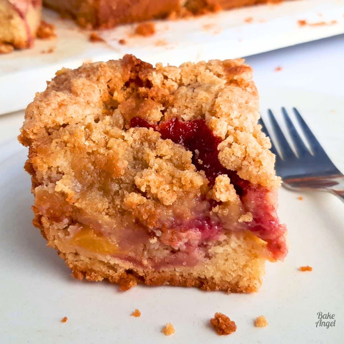 Close up of a slice of fruit crumble cake showing the strawberries and peach inside.