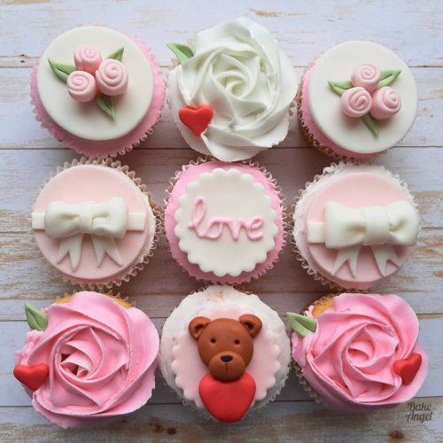 A set of cupcakes decorated with homemade marshmallow fondant, and buttercream icing. There are fondant bows, mini roses and a teddy bear with heart details.