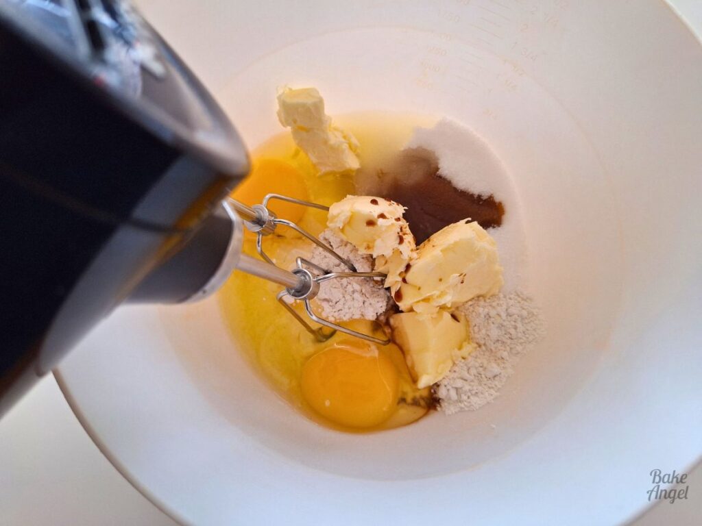 Making vanilla cake batter in a bowl with a hand mixer for peach upside down cake.