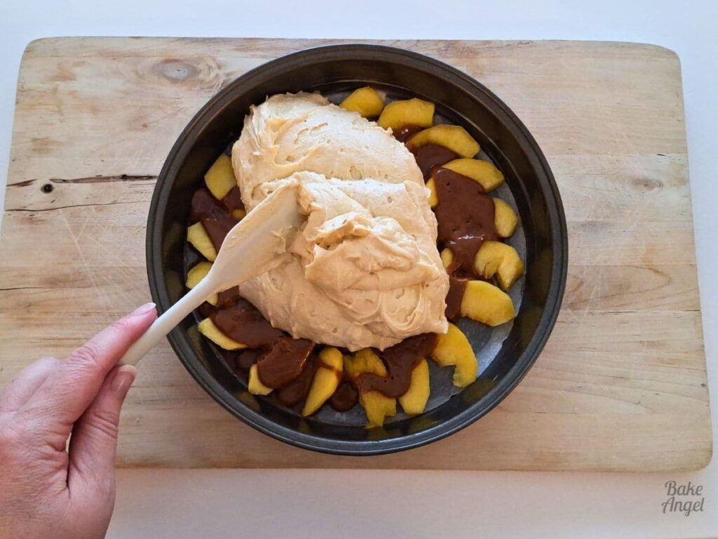 Cake batter spread over caramel peaches with a spatula before baking.